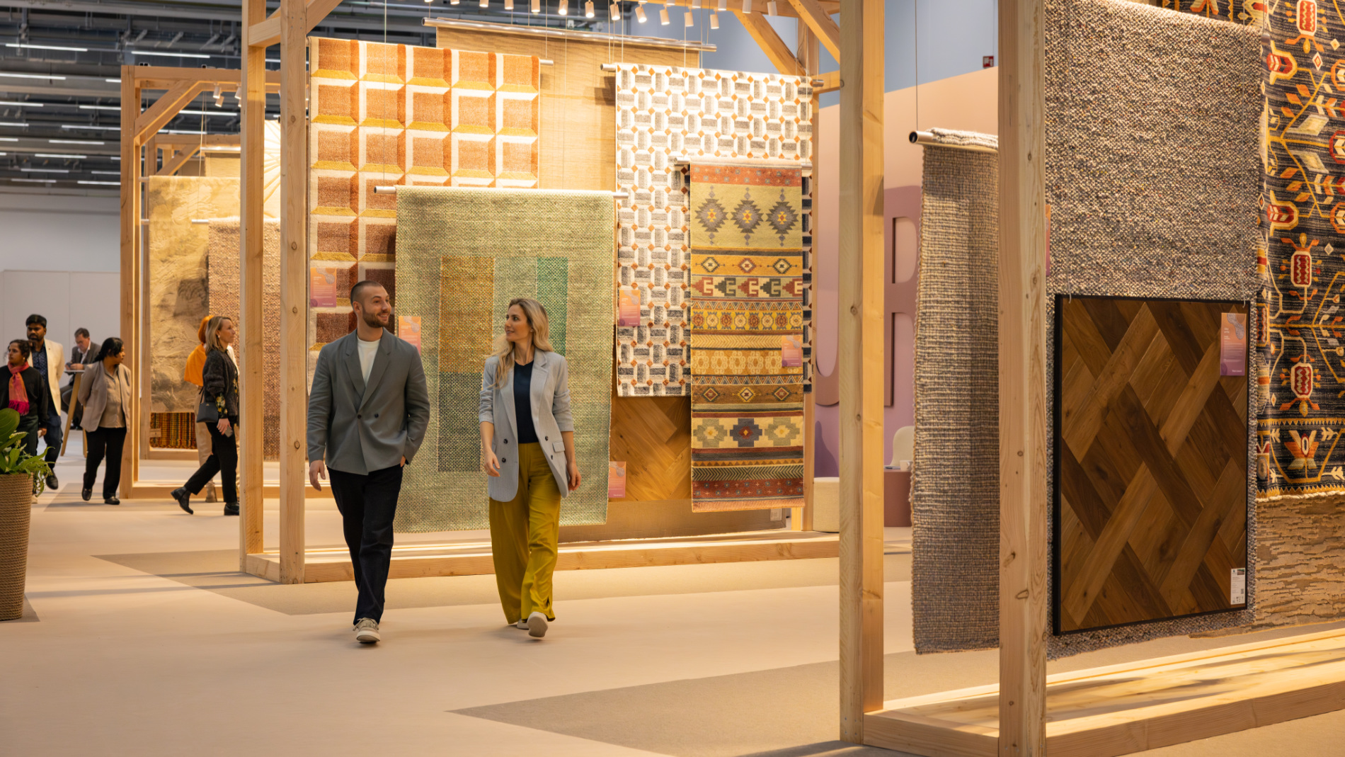 Two visitors walk through an exhibition booth featuring large rugs and flooring samples